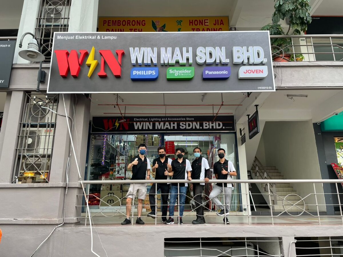 Grey WIN MAH SDN. BHD. signboard with Philips, Schneider Electric, Panasonic and Joven logos above a shop entrance, staff standing on the walkway