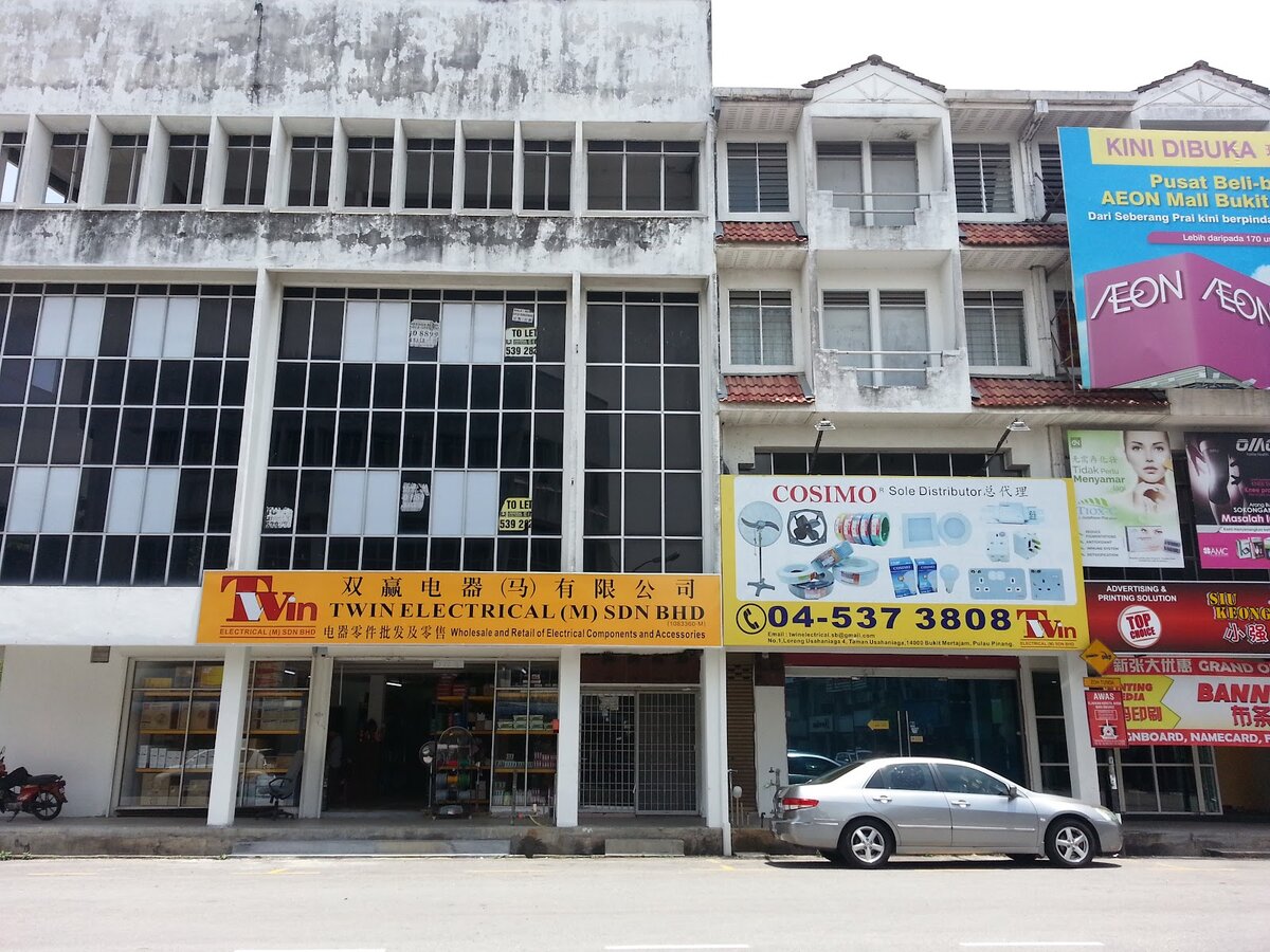 Row of shophouses with a yellow Twin Electrical signboard, a Cosimo board showing fans, cable rolls, sockets and bulbs, and the phone number 04-537 3808