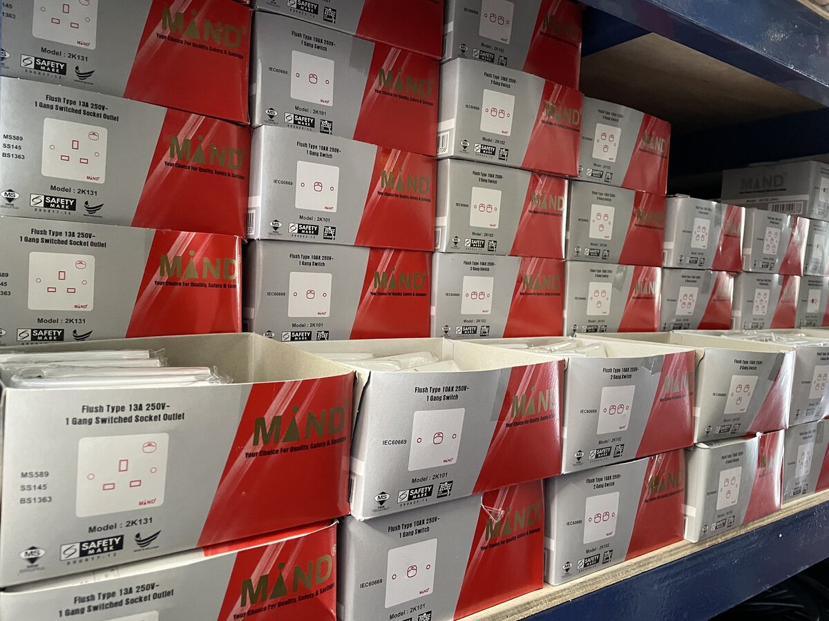 Shelf stacked with red-and-silver Mand boxes of one-, two- and three-gang switches and 13 A switched socket outlets