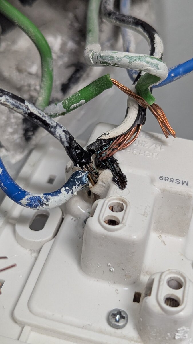Back of a white three-pin socket outlet with blackened, melted wire insulation and frayed copper strands at the terminals