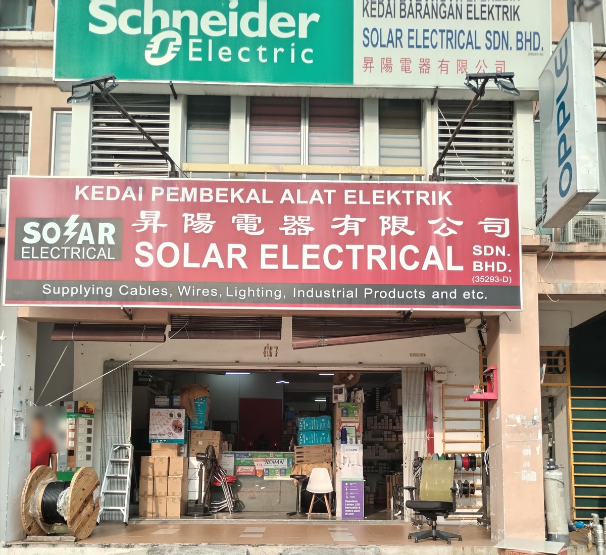 Shopfront with a red Solar Electrical signboard and a green Schneider Electric sign above, cable drum and boxes at the open door