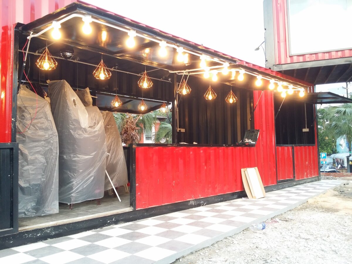 Red shipping-container café with string lights and pendant lamps along the roof edge