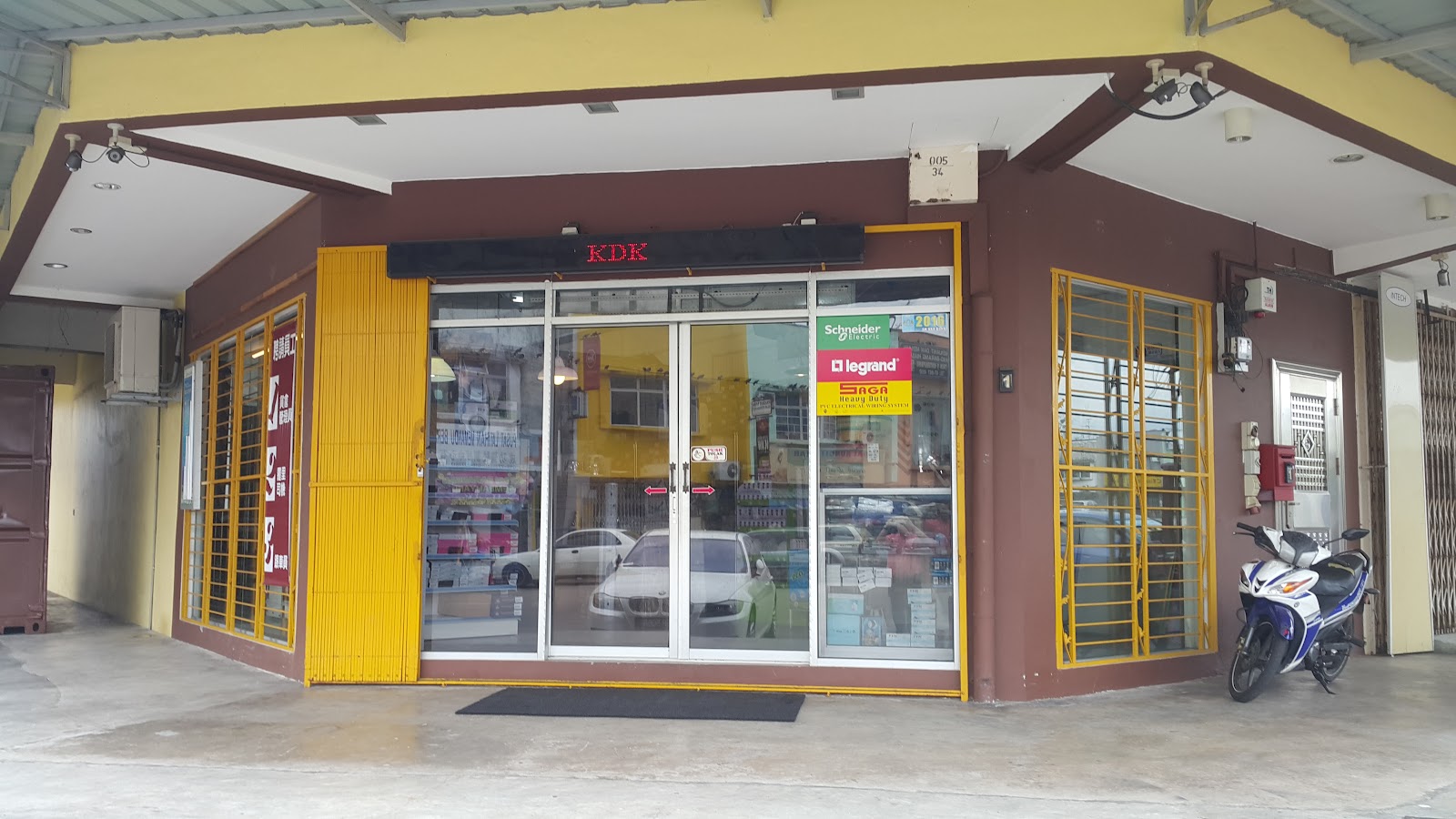 Corner shop with yellow window grilles and glass doors bearing Schneider Electric, Legrand and Saga stickers