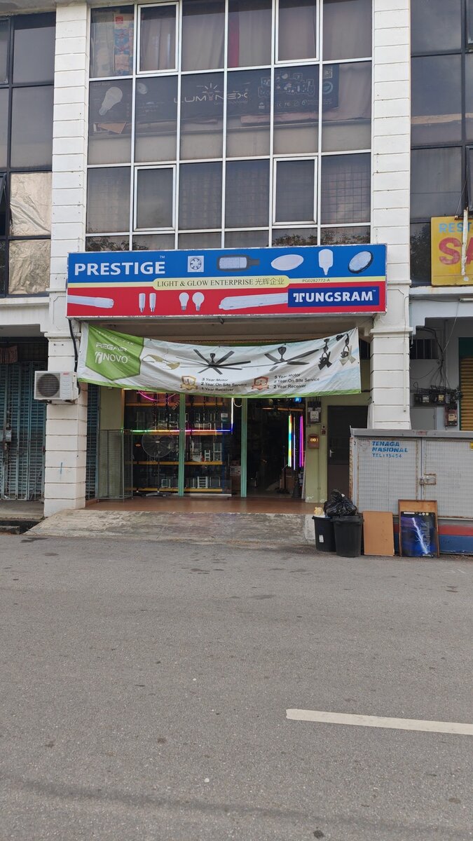 Shop lot with a blue and red signboard showing lamps, the words Prestige, Light & Glow Enterprise and Tungsram, and a ceiling-fan banner over the entrance