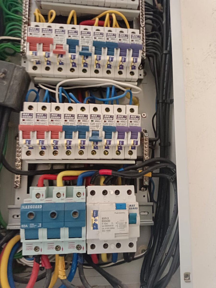 Open three-phase distribution board with two rows of Maxguard miniature circuit breakers in red, blue and purple above a blue three-pole isolator and a four-pole residual current circuit breaker