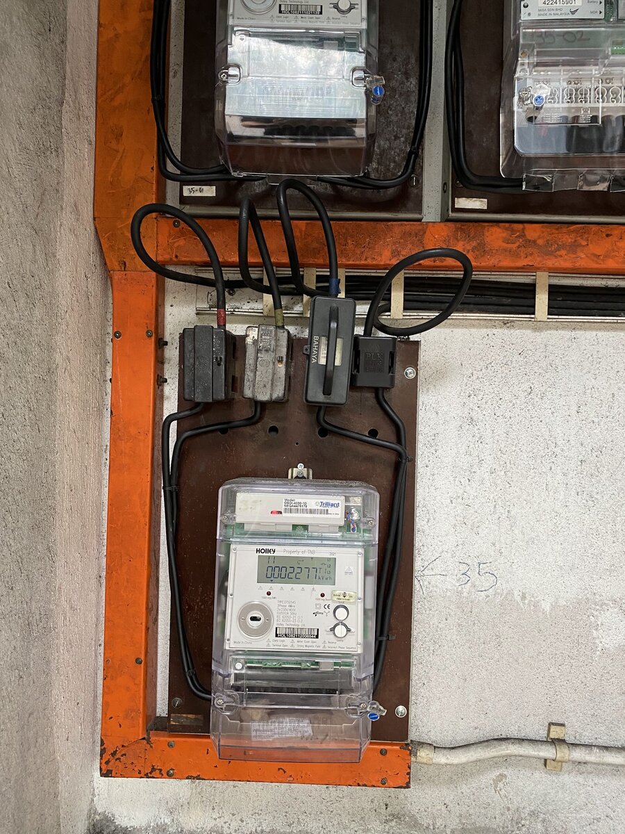 Electricity meter and cut-out fuses on a wooden board with black cables, framed in orange trunking