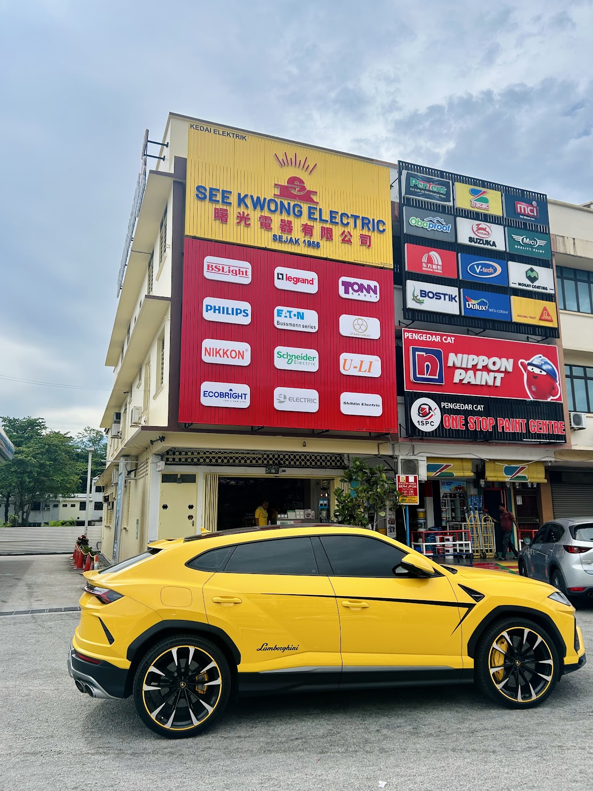 Corner shophouse with a yellow See Kwong Electric signboard and a red wall of brand logo panels