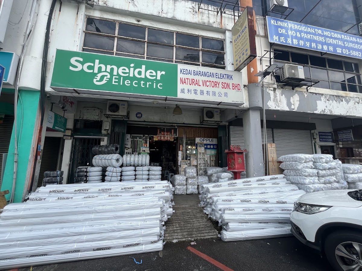 Shop with a green Schneider Electric and Natural Victory signboard and bundles of white conduit stacked on the pavement