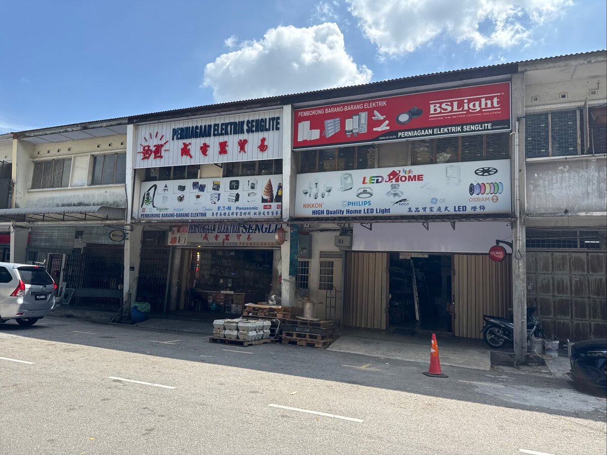Two-unit shophouse front with a white Perniagaan Elektrik Senglite sign, a red BSLight sign and printed panels of electrical products and brand logos