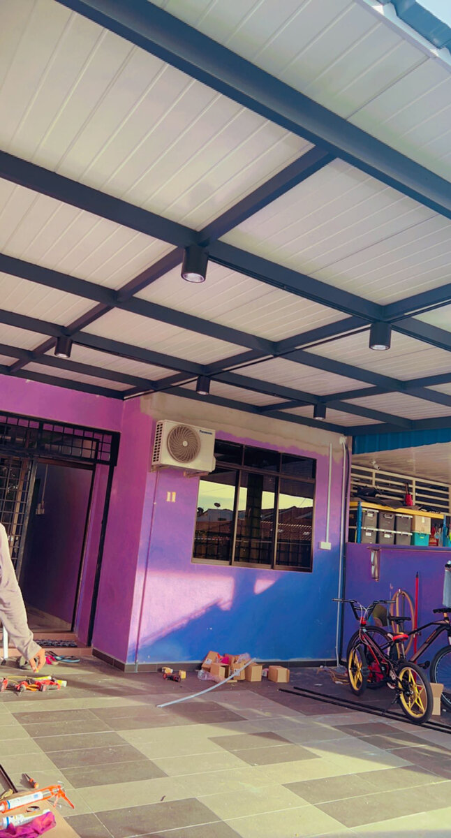 Porch with a white metal-deck roof on dark beams fitted with small black ceiling spotlights, a wall-mounted aircond unit and two bicycles below