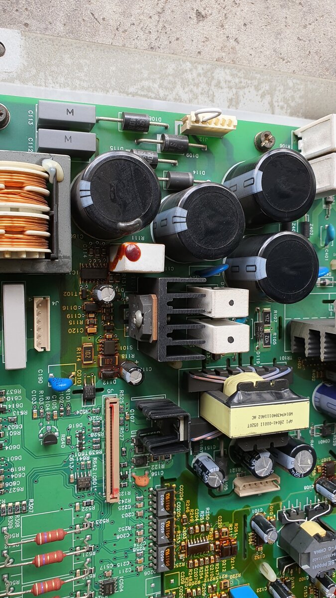 Green printed circuit board with four large black capacitors, a copper-wound choke, heat sinks and connectors