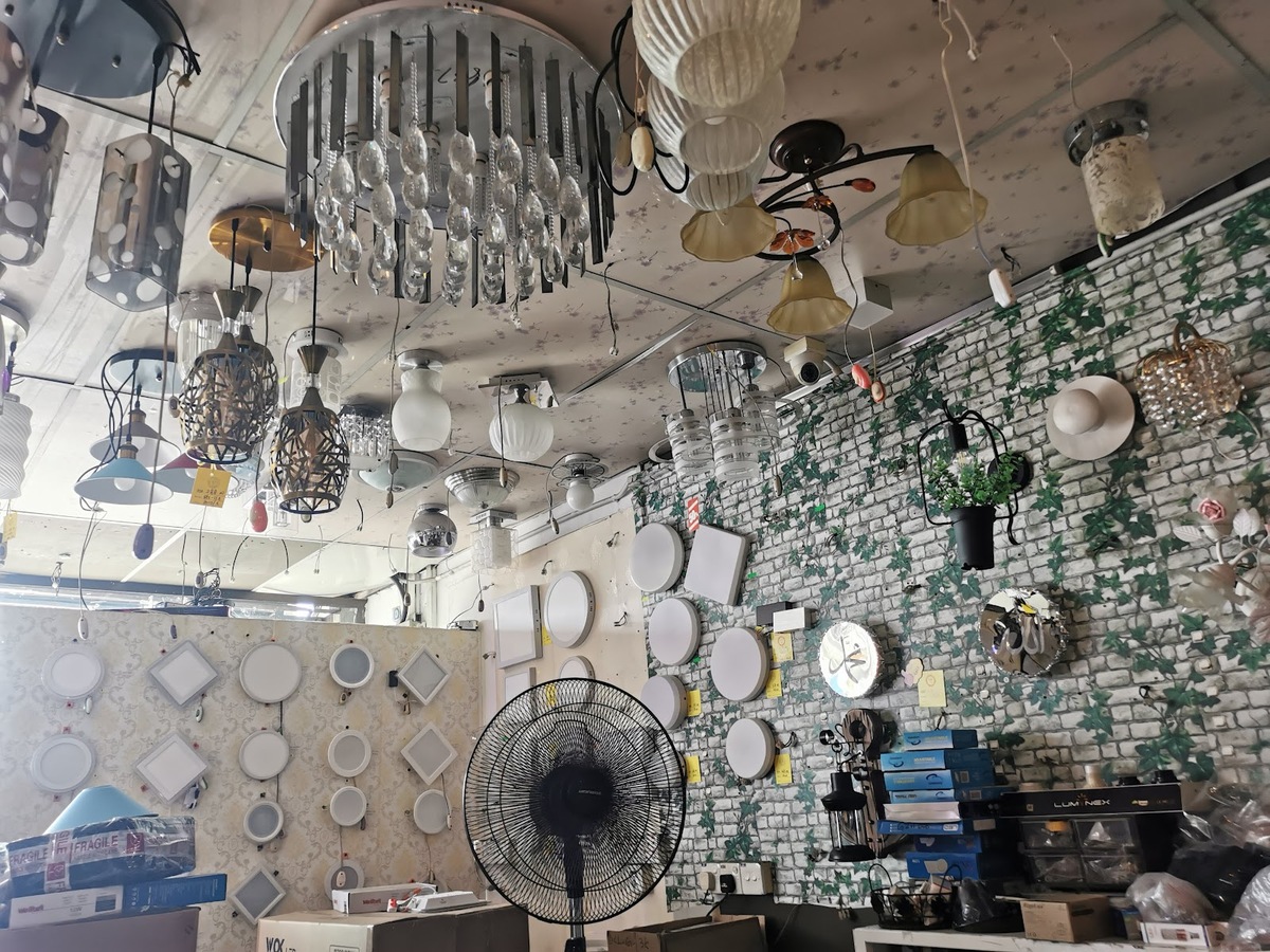 Ceiling hung with pendant and crystal lamps, walls lined with round and square ceiling panel lights and a black stand fan in front