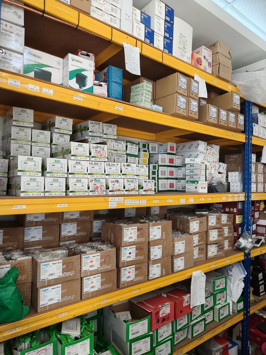 Yellow shelving packed with boxed EPS breakers, Hager Muse switch cartons, Schneider and Legrand boxes