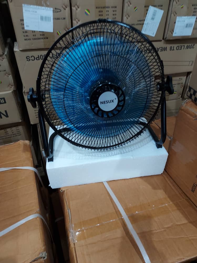 Black and blue Nesux table fan on a foam block in front of stacked brown cartons