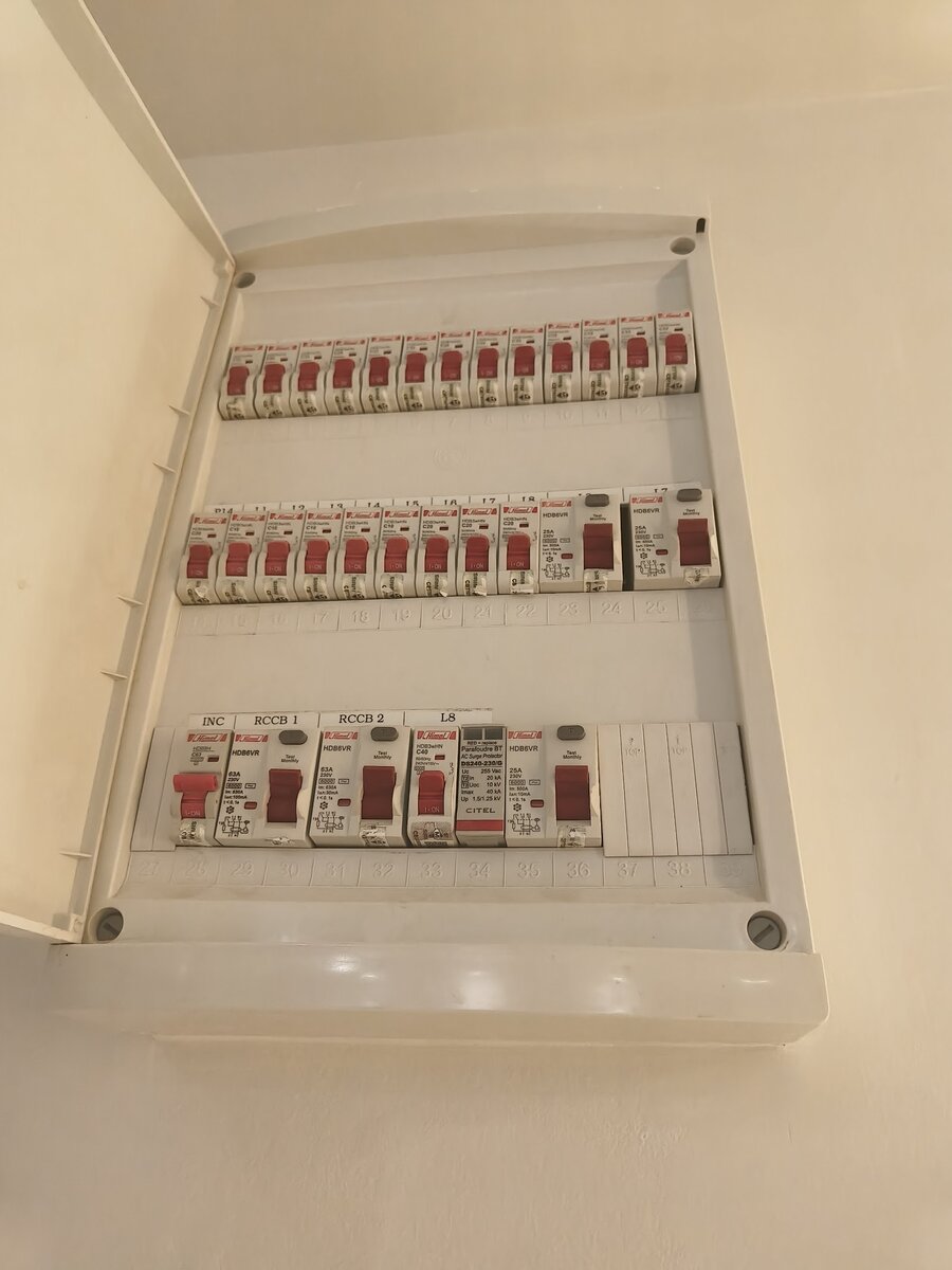 Open white distribution board with three rows of red-labelled Himel miniature circuit breakers and RCCBs, labelled INC, RCCB 1 and RCCB 2, and a grey surge protector module
