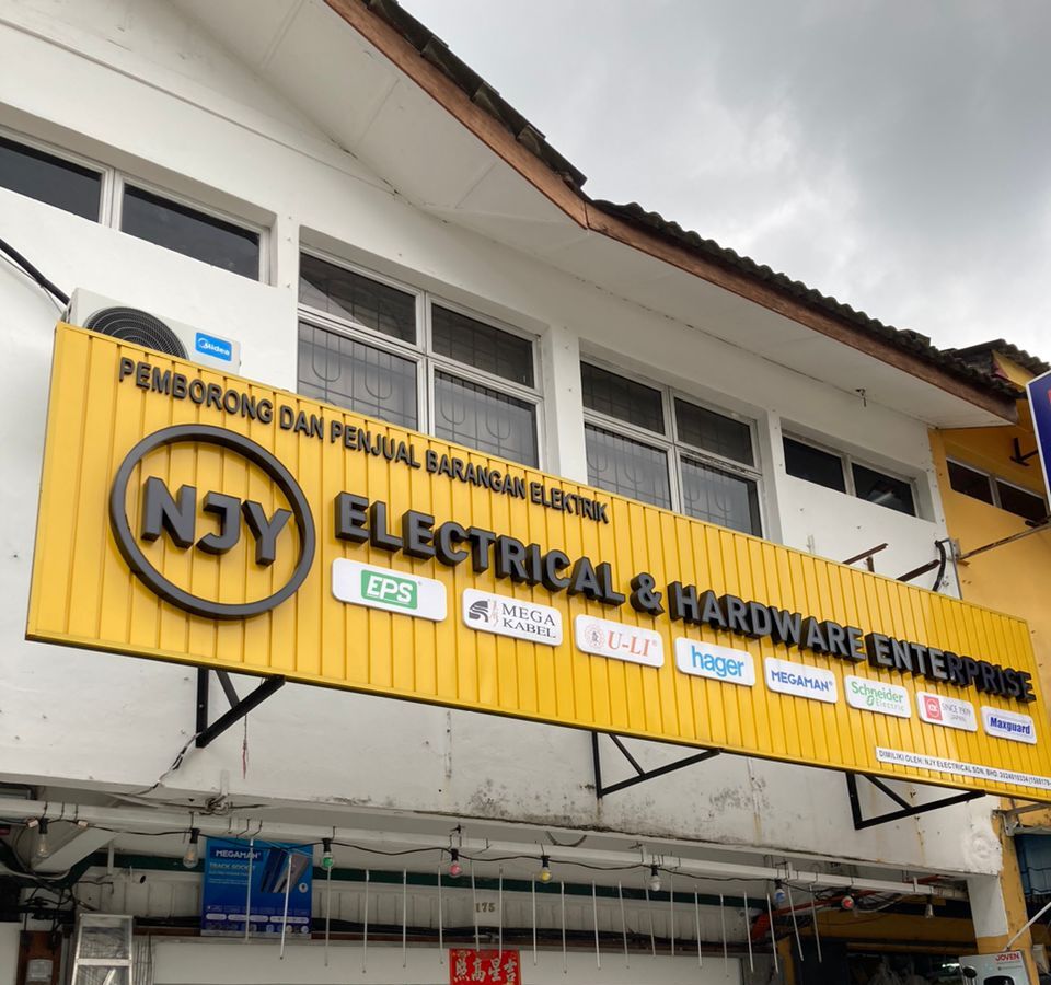 Yellow signboard on a white shophouse reading NJY Electrical & Hardware Enterprise, with logos including EPS, Mega Kabel, U-Li, Hager, Megaman, Schneider Electric and Maxguard