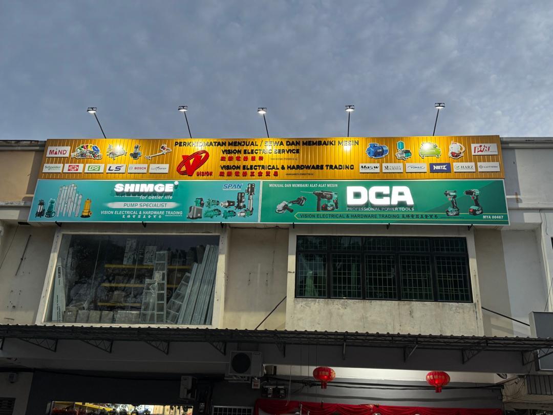 Two-storey shophouse with a lit yellow signboard reading Vision Electric Service and Vision Electrical & Hardware Trading, brand logos, and green Shimge and DCA panels below