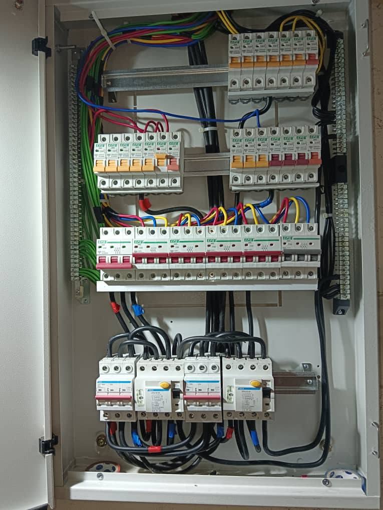 Large open metal distribution board with two rows of single-pole breakers, a row of three-pole breakers fed by red, yellow and blue cables, and four larger devices at the bottom