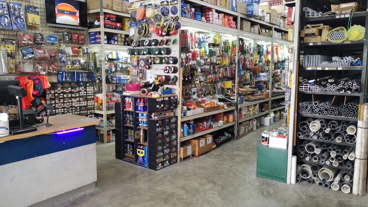 Hardware shop interior with a counter, pegboards of tools and cutting discs, shelves of fasteners and a rack of PVC and metal pipes