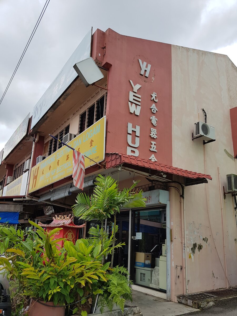 Corner shophouse with a vertical Yew Hup sign in white letters on a red wall, potted plants and a glass shop door