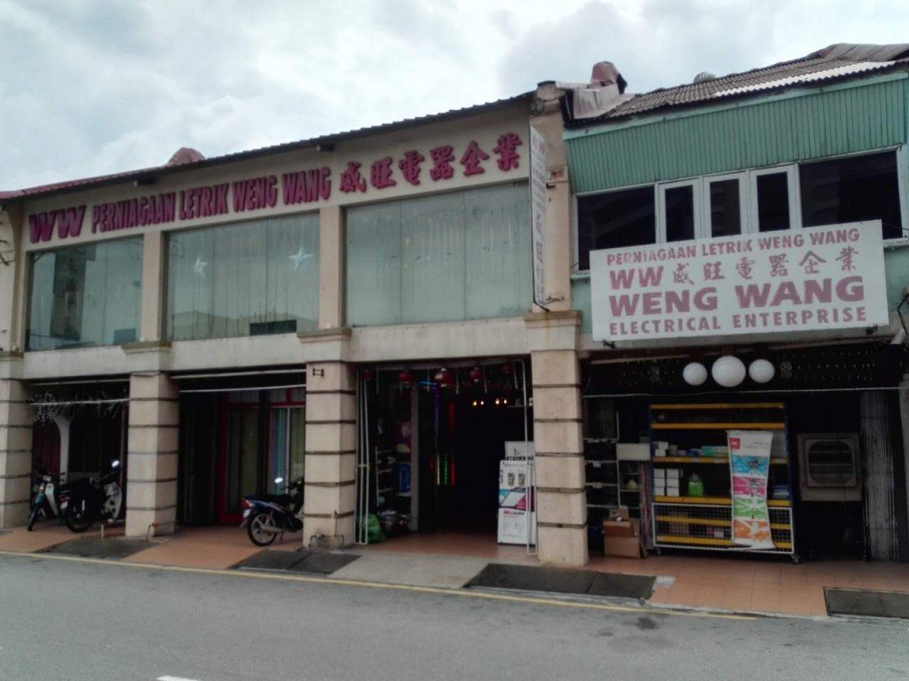 Row of old shophouses with red signboards reading Perniagaan Letrik Weng Wang and Weng Wang Electrical Enterprise, with goods displayed at the five-foot way