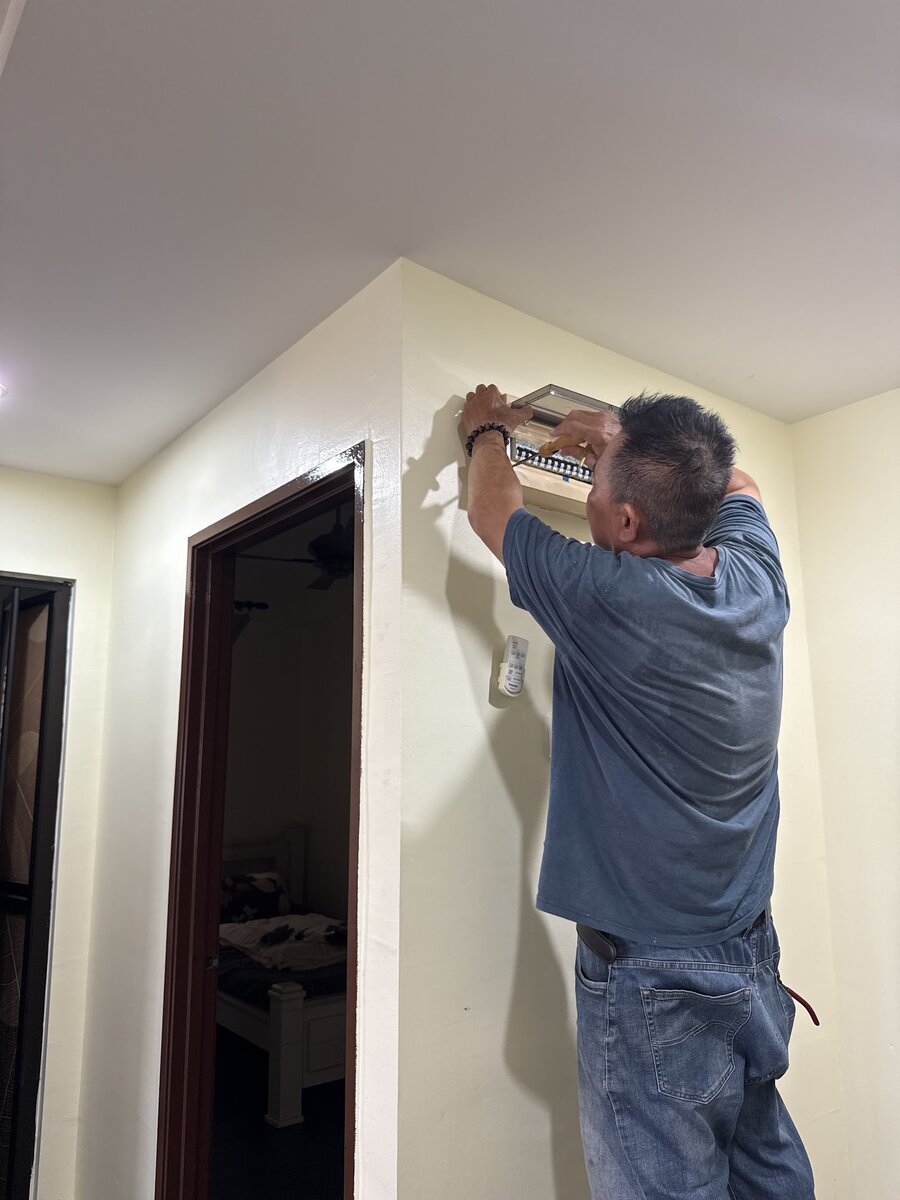 Man standing beside a door, reaching up to an open distribution board mounted high on a white wall