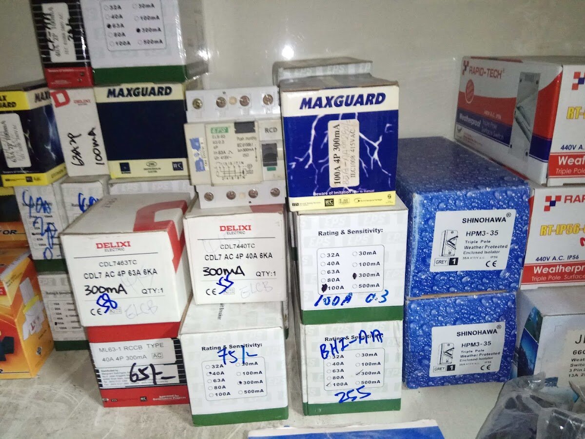 Stacked boxes of residual current circuit breakers and weatherproof isolators, one RCCB unboxed, with handwritten codes on the boxes