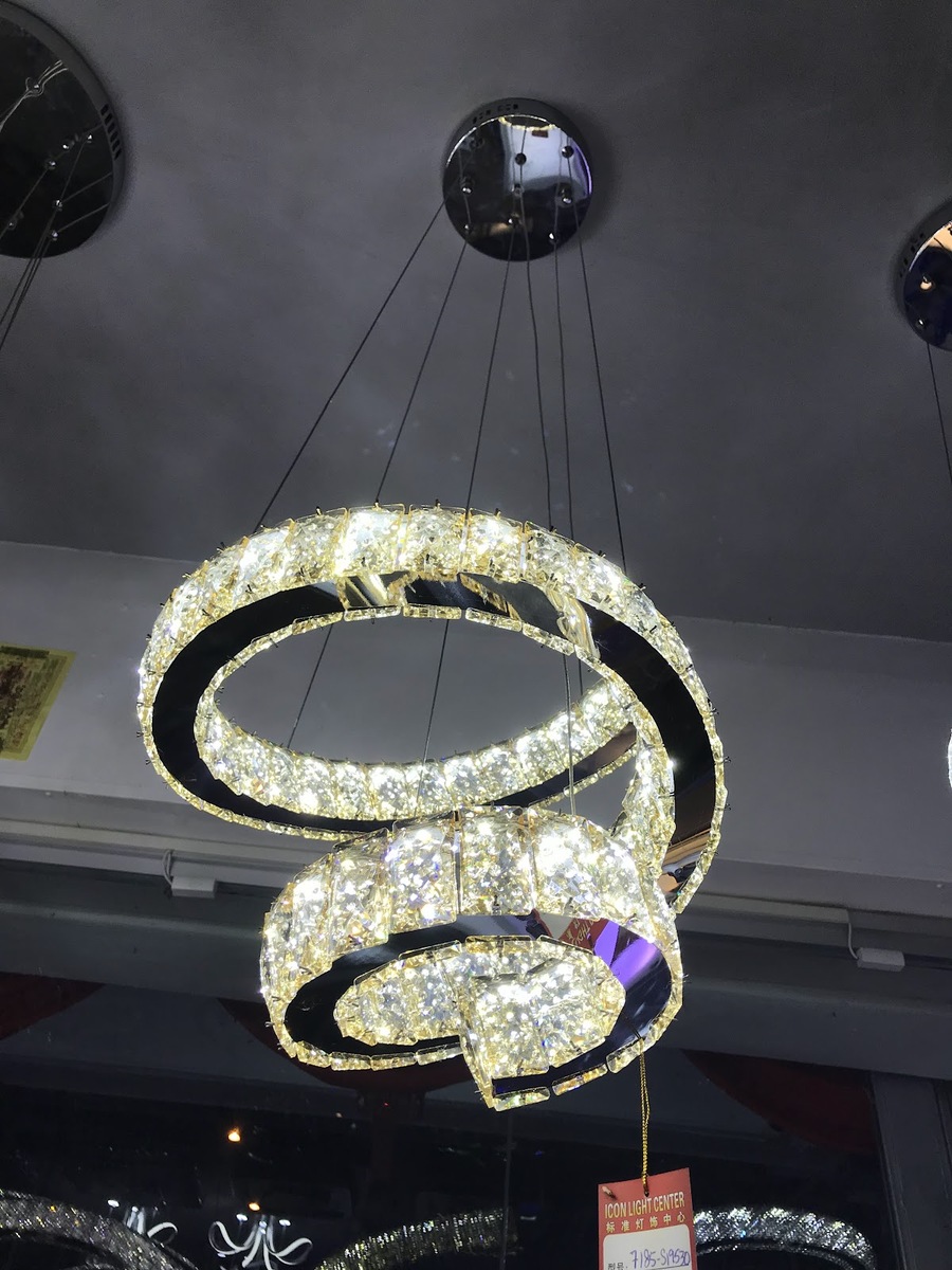 Two-tier ring chandelier of glowing crystal blocks hanging from a chrome ceiling plate, with a red shop tag below