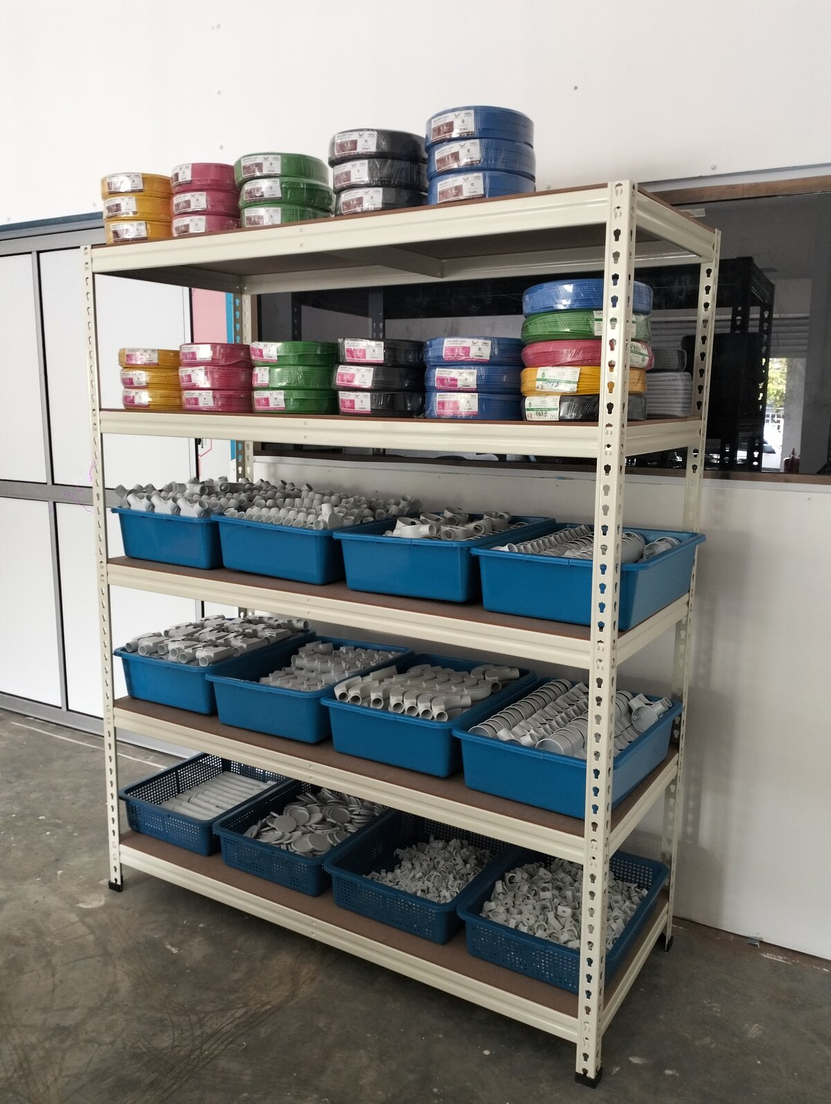 Metal shelf with coloured cable coils in yellow, red, green, black and blue on two levels and blue baskets of white conduit fittings below