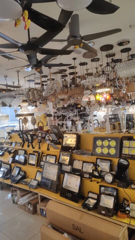 Shop interior with black ceiling fans and lights hanging from the ceiling above a yellow display wall of floodlights