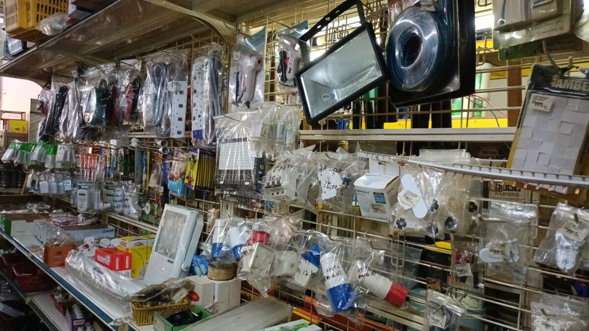 Wire display racks hung with extension sockets, a halogen floodlight, bagged blue and red industrial plugs, lamp holders and an emergency light