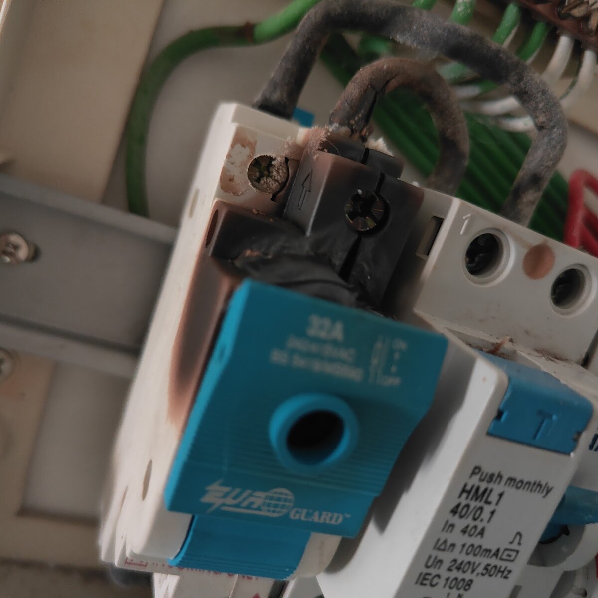 Close-up of a distribution board: a blue-toggled 32 amp isolator blackened by heat at its terminals, next to a white residual-current circuit breaker