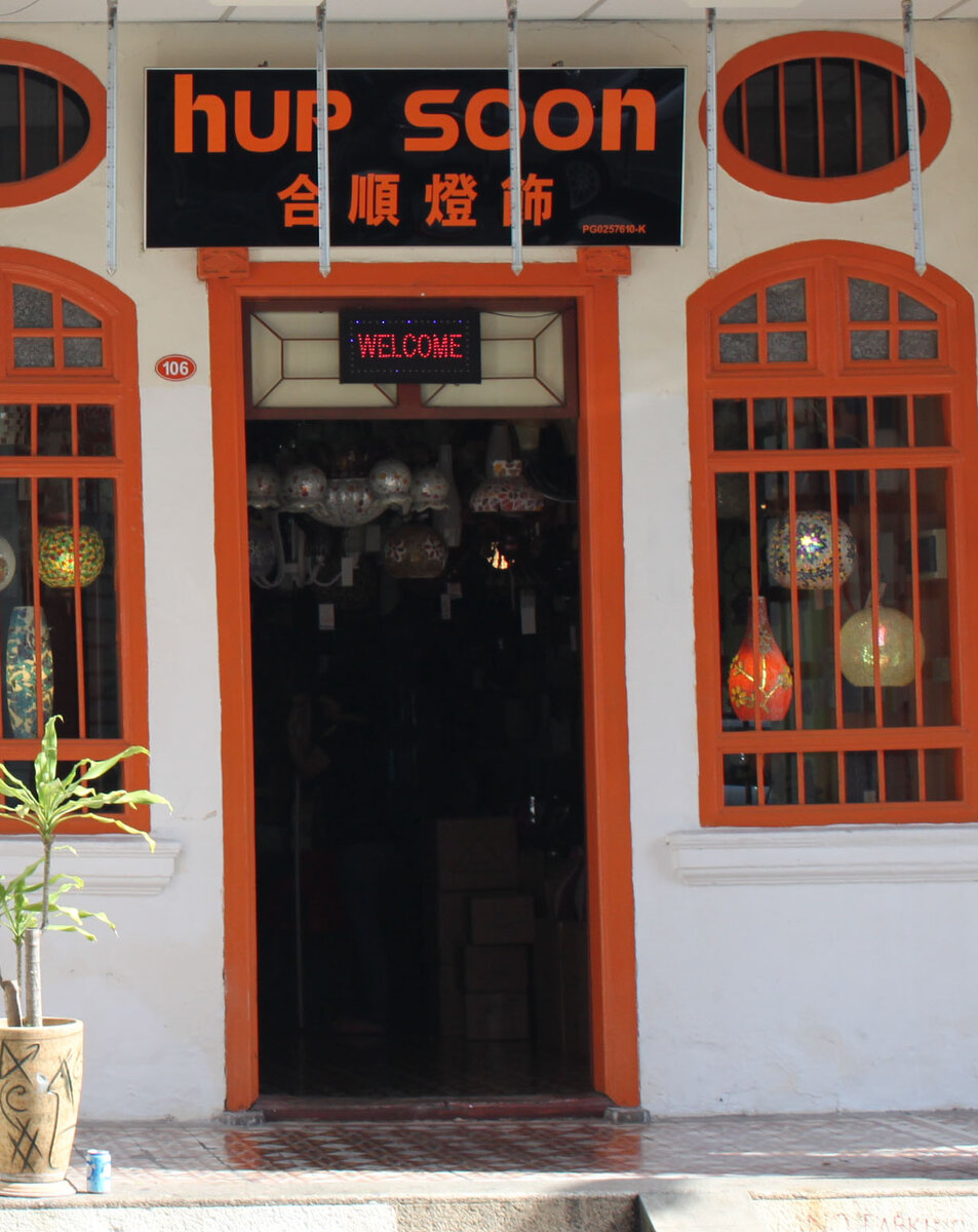Shophouse doorway with orange window frames, a black signboard reading Hup Soon in orange letters, and hanging lamps visible inside