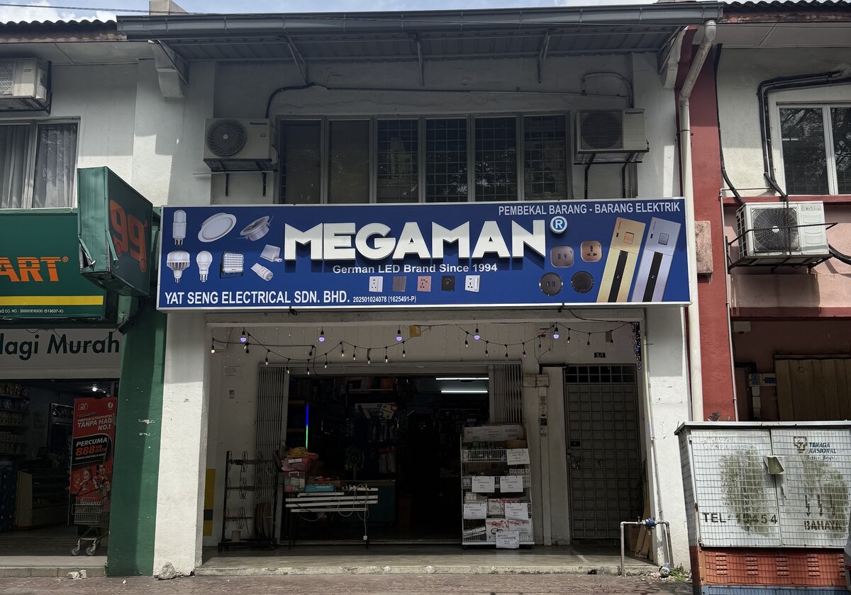Two-storey shophouse with a blue Megaman signboard reading Yat Seng Electrical Sdn. Bhd., an open shopfront with a rack of boxed goods, and a 99 Speedmart next door
