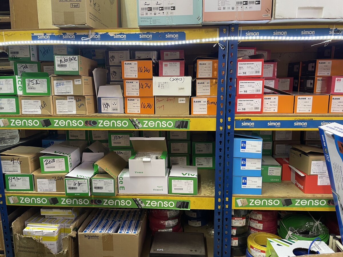 Steel shelving with Simon and Zenso shelf strips, stacked orange, red, green and blue switch boxes, and coils of red, black, yellow and green wire on the lowest shelf