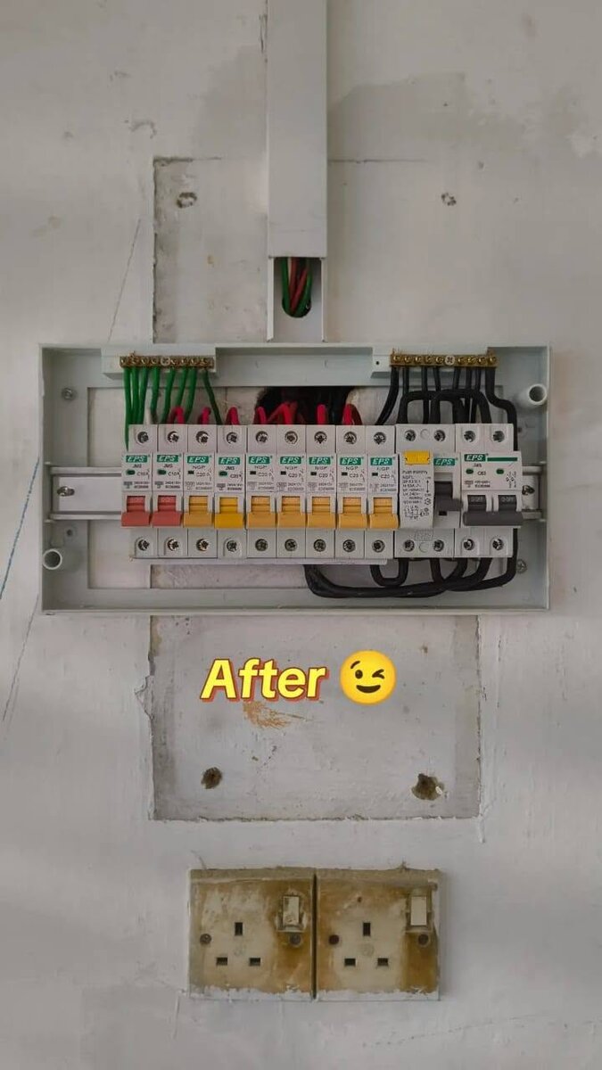 Grey DB box with its cover off on a white wall with patched plaster, a row of EPS breakers with red, orange and grey toggles, a trunking run entering from above, the word After with a winking emoji, and two old twin sockets below