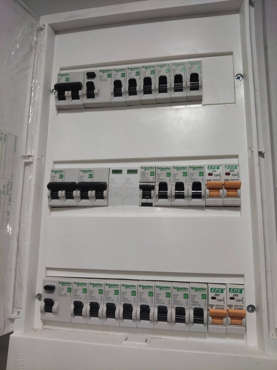 Open white surface-mounted distribution board with three rows of Schneider breakers and a few orange EPS breakers