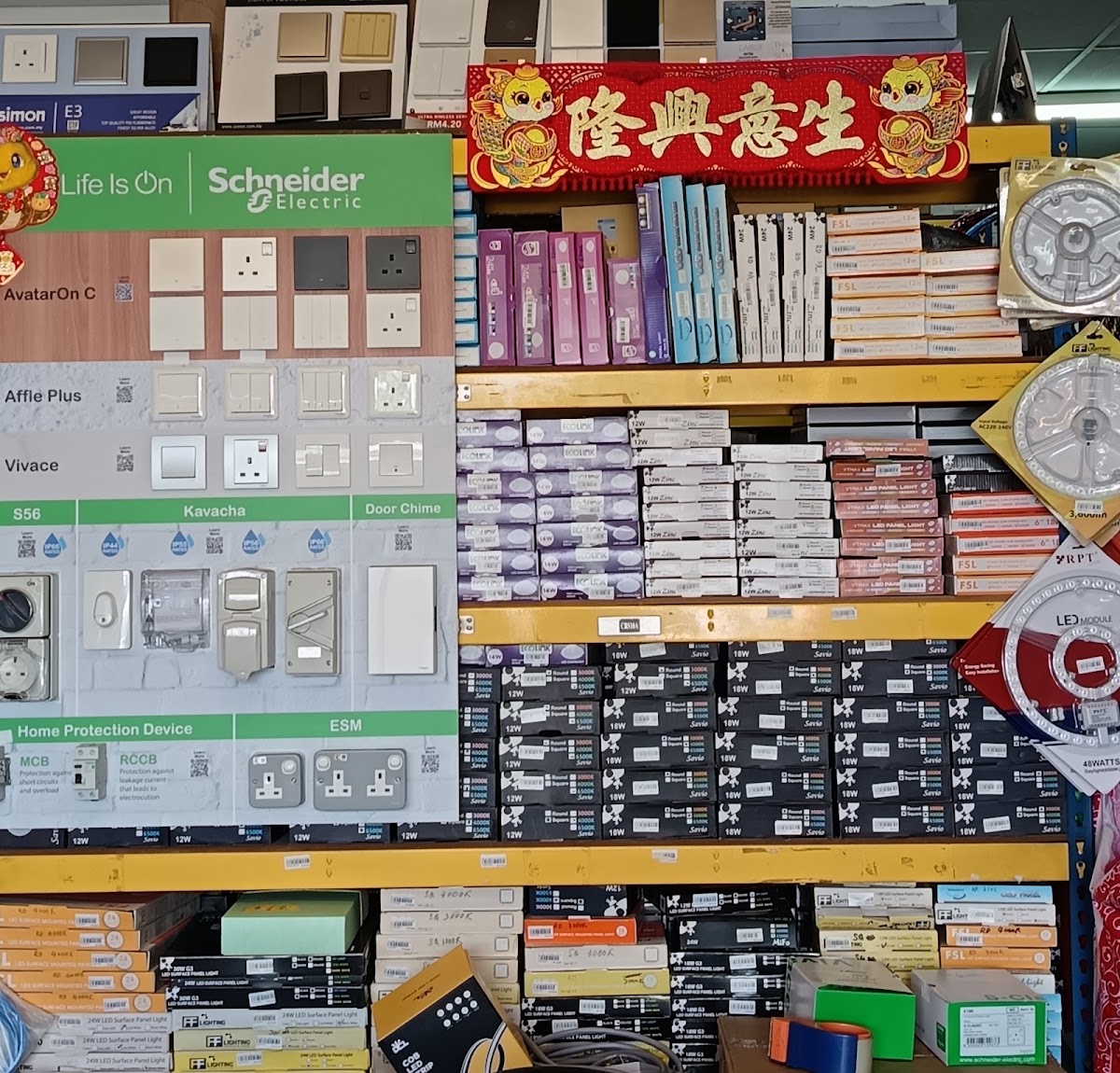 Schneider Electric display board with switch and socket samples next to shelves stacked with boxed LED panel lights and hanging LED ceiling modules