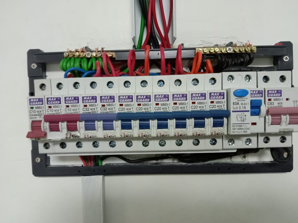 Distribution board with a row of purple-labelled Maxguard miniature circuit breakers, an RCCB with a blue test button and a two-pole main switch, with cables entering through trunking above