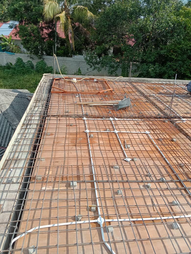 Concrete-slab formwork with steel reinforcement mesh and white electrical conduits running to light-point boxes, trees behind