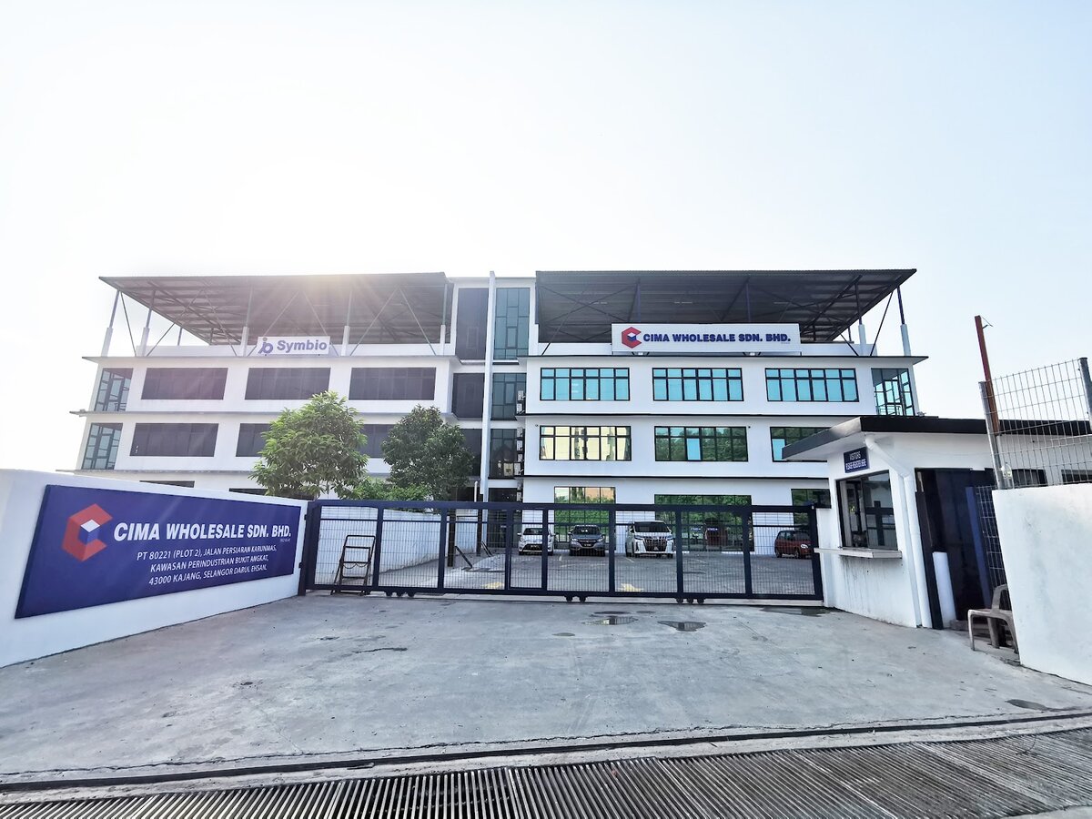 Three-storey white industrial building with a "Cima Wholesale Sdn. Bhd." sign on the façade and a blue Cima Wholesale wall sign at the gate