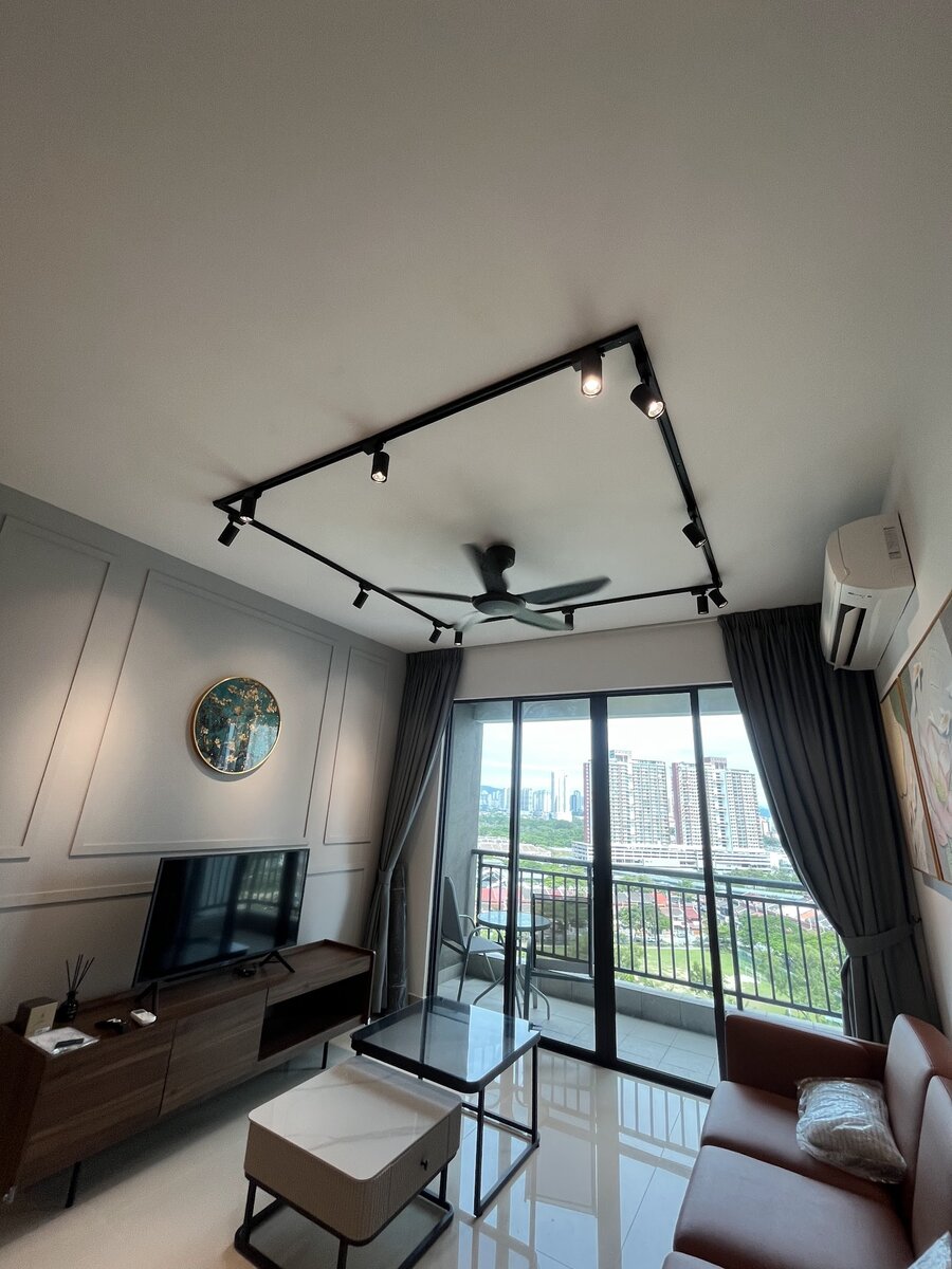 Condominium living room with a black rectangular ceiling track of spotlights around a ceiling fan, a wall aircond and a balcony overlooking apartment blocks