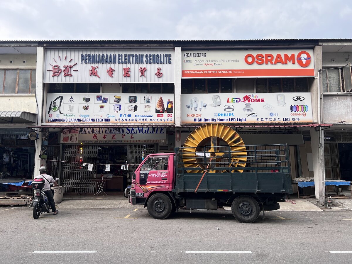 Shopfront with Perniagaan Elektrik Senglite and OSRAM signs, brand panels and a lorry carrying a large yellow cable drum