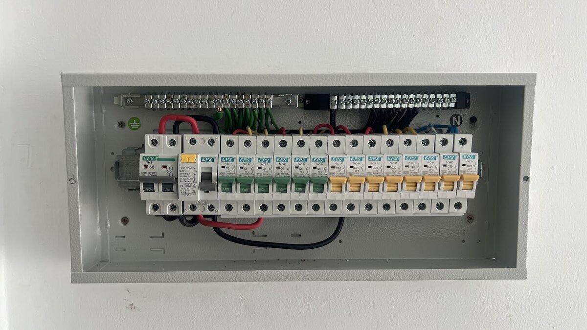 Open grey distribution board with a double-pole main switch, an RCCB and a single row of six green and eight yellow miniature circuit breakers below the earth and neutral bars