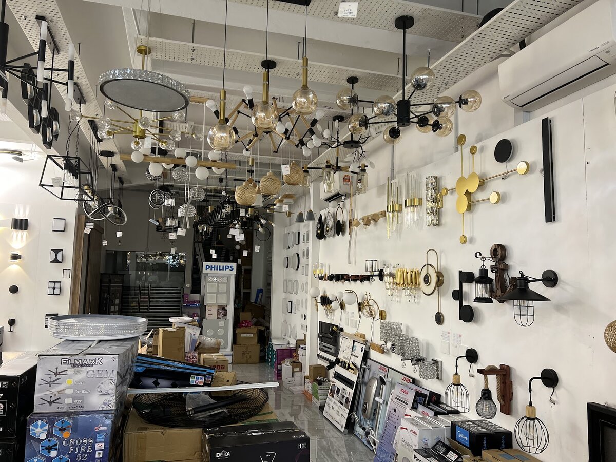 Shop interior crowded with hanging pendant lights and chandeliers, wall lights along the right wall and boxed fans on the floor