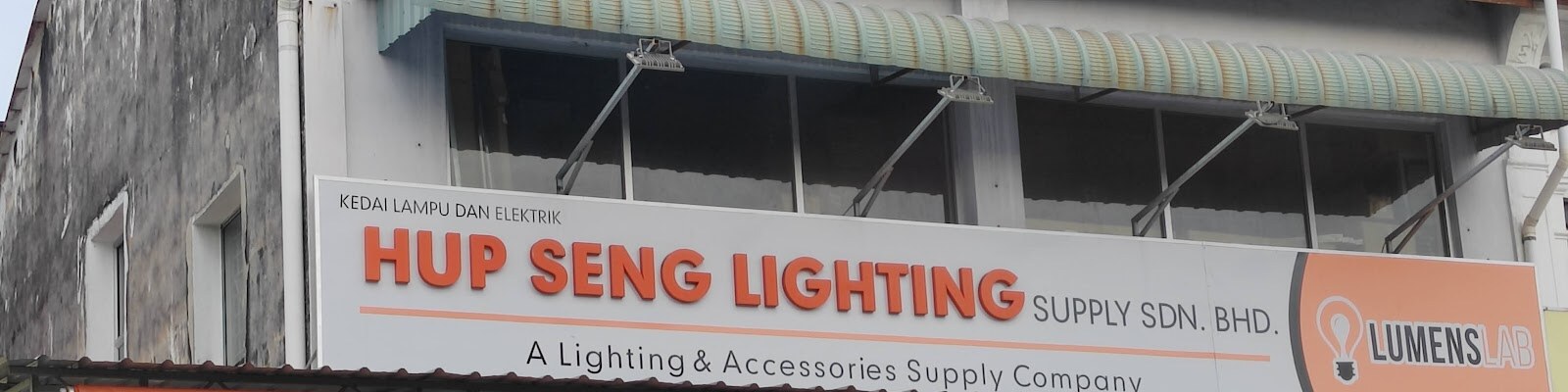 Shop signboard reading Hup Seng Lighting Supply Sdn Bhd with an orange Lumens Lab panel on the right