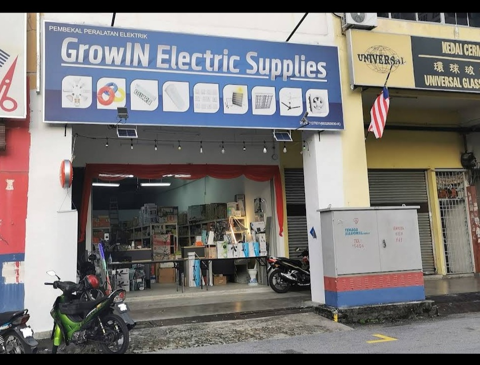 Shopfront with a blue GrowIN Electric Supplies signboard showing product icons, an open front with shelves of boxed goods and motorcycles parked outside