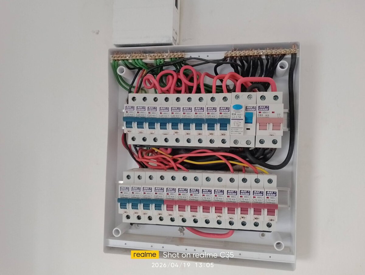 Open white distribution board with a row of nine blue-toggle Maxguard C20 MCBs, a Maxguard RCCB with a blue test button and a pink two-pole MCB, a second row of MCBs below and red cables looped between them