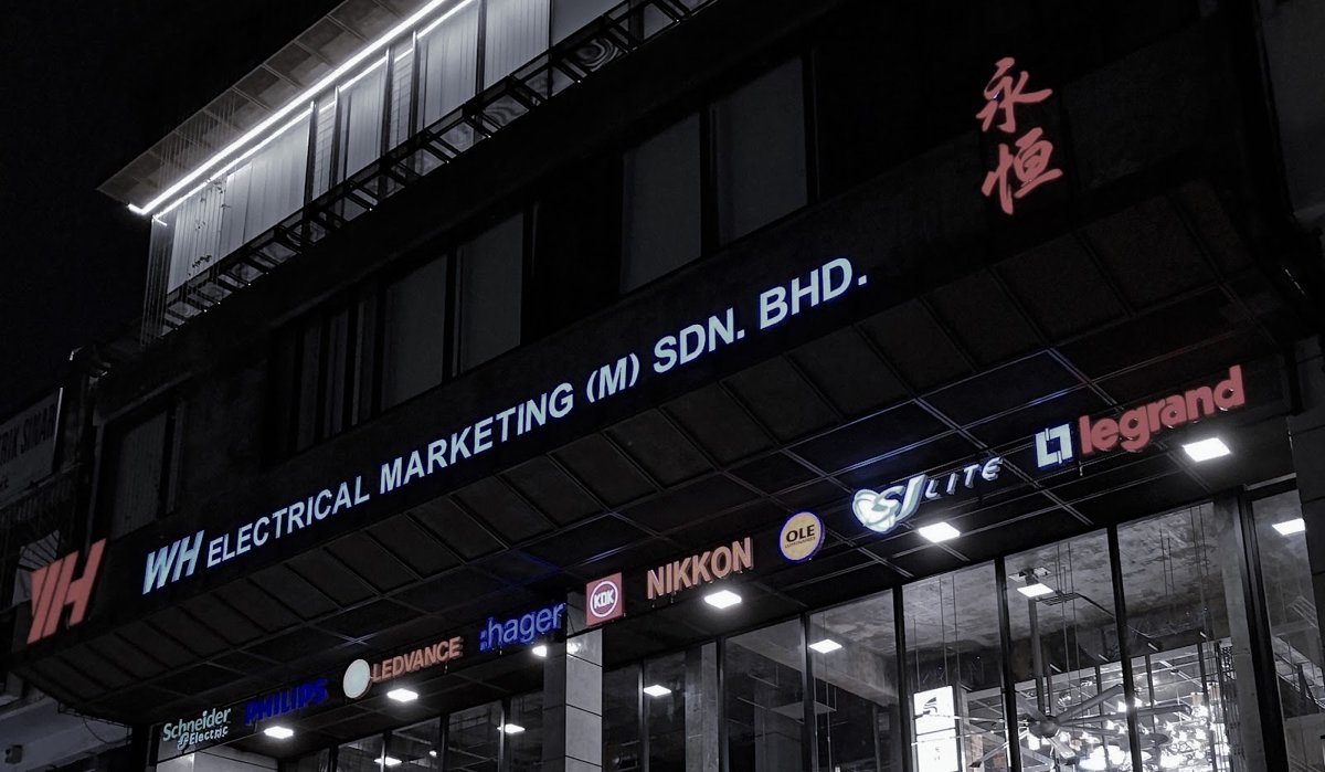 Illuminated fascia reading WH Electrical Marketing (M) Sdn. Bhd. with a row of brand logos including Schneider Electric, Philips, Ledvance, hager, KDK, Nikkon and legrand over a glass shopfront