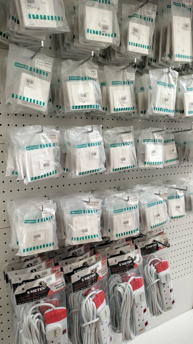 Pegboard of bagged white Siemens wall switches and sockets with price stickers, above packs of 5-metre extension trailing sockets